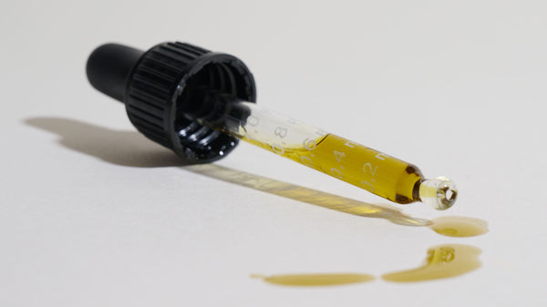 A CBD oil dropper with golden oil and millilitre markings, a drop falling onto a clean surface.