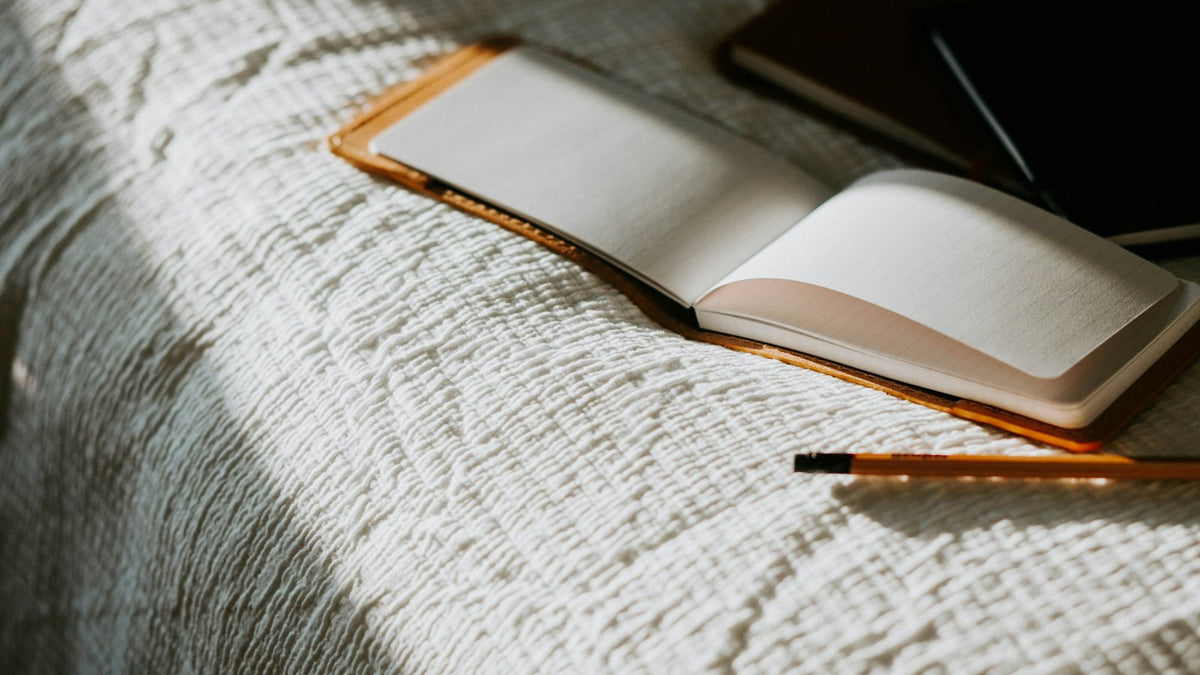 An open notebook and a pencil on a bed