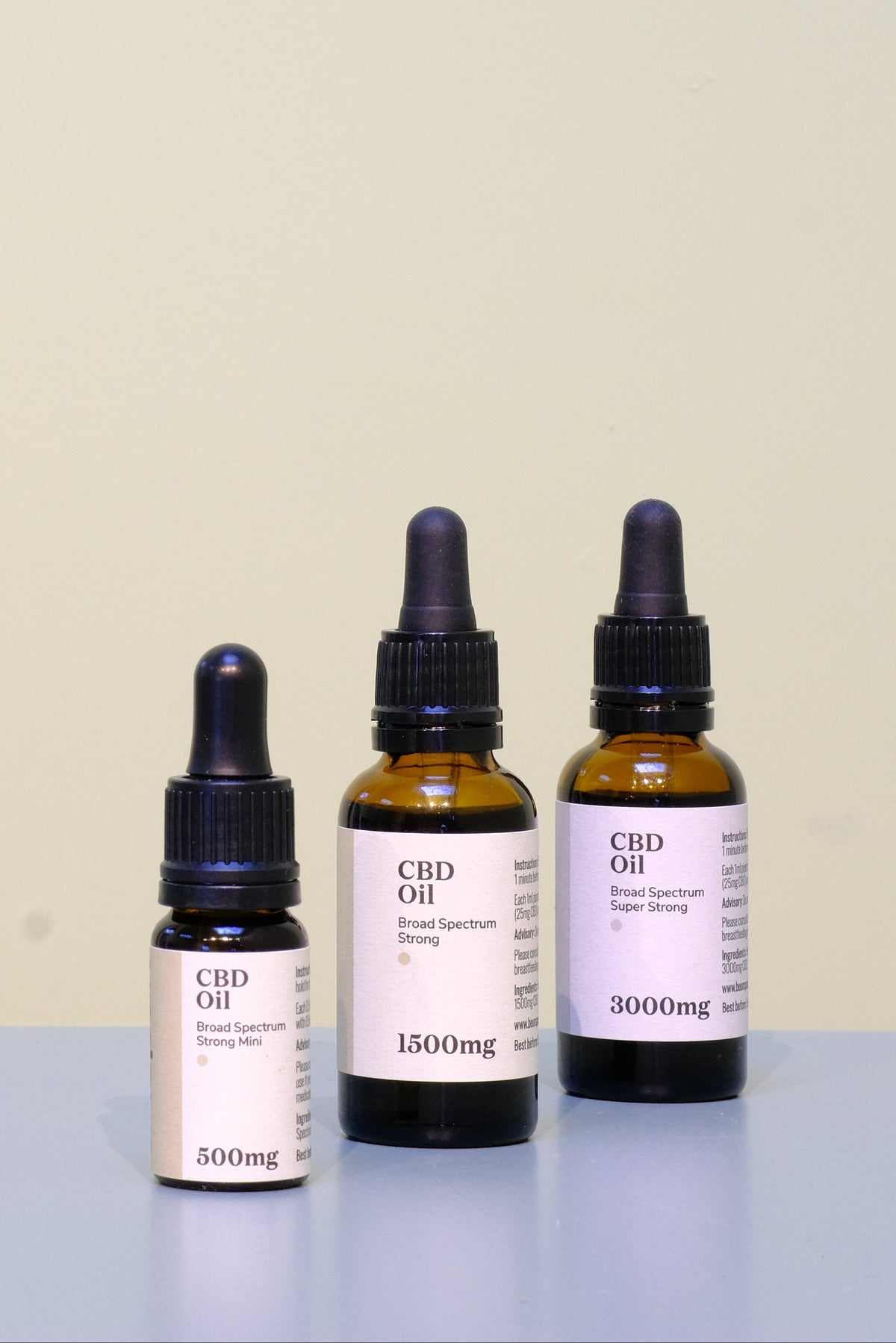 Three CBD oil bottles with varying dosages on a light surface and beige background