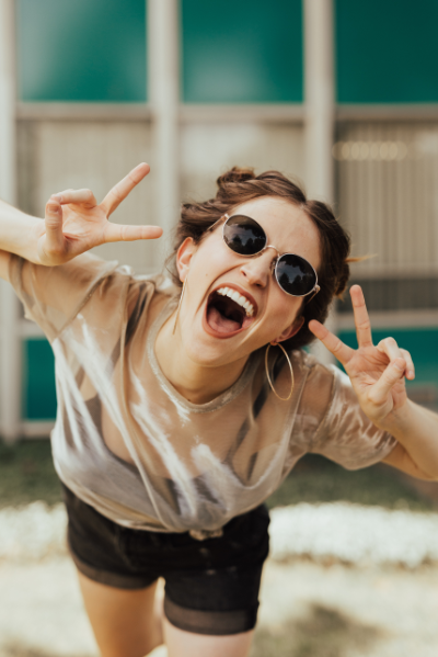 A joyful woman in round sunglasses and a casual outfit throws up peace signs with both hands. Her exuberant expression and playful pose convey excitement, matching the section's message about the convenience of free delivery on all orders using Royal Mail Tracked 48, ensuring customer satisfaction and carefree shopping experience.